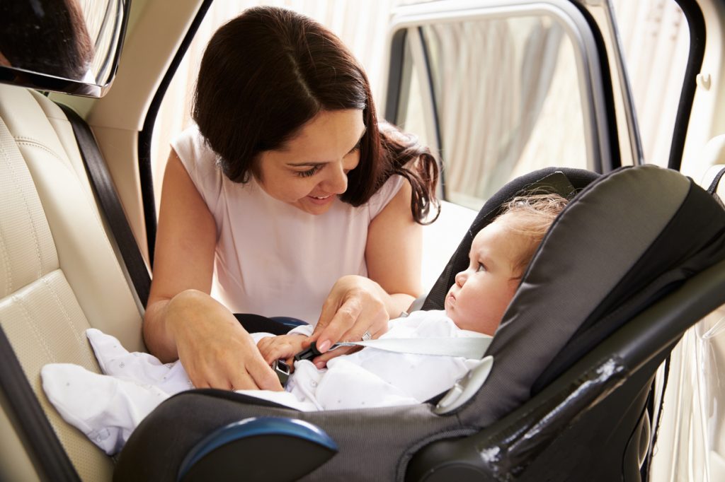 Mother putting baby son into car travel seat