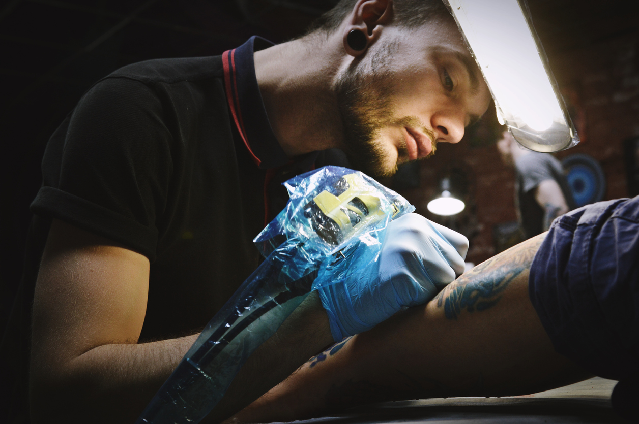 Beautiful tattooist with tunnels makes a tattoo on his leg